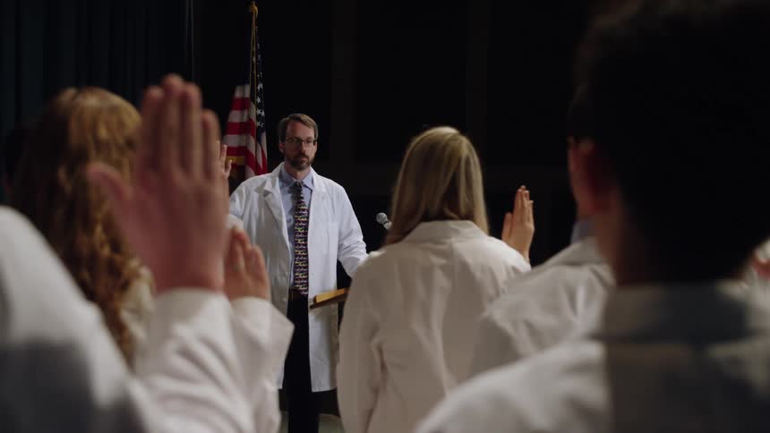 Doctor in white coat administers hippocratic oath to others