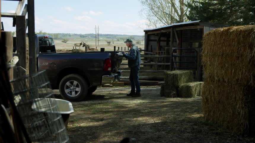 An older white man closes the rear of a truck on a farm