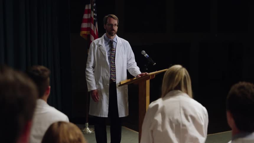 A man stands on stage as the audience stands up and they take an oath