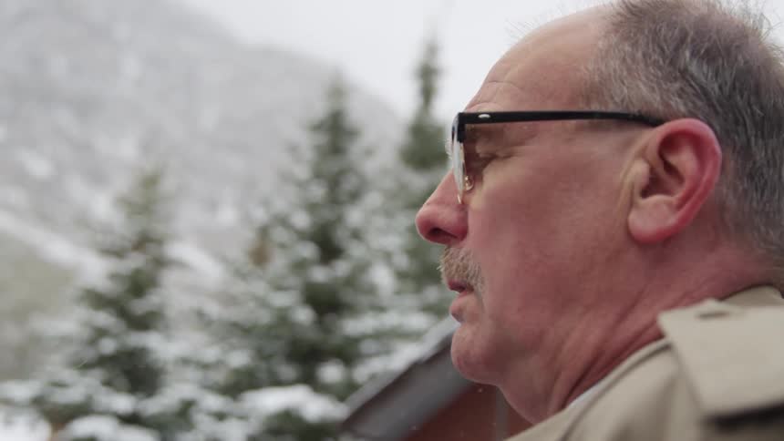 Elderly man with a mustache and glasses stands and closes his eyes when it snows
