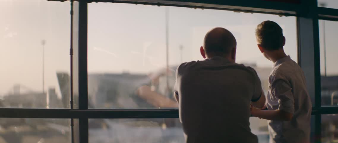 A man and a boy in an airport talking and looking at airplanes
