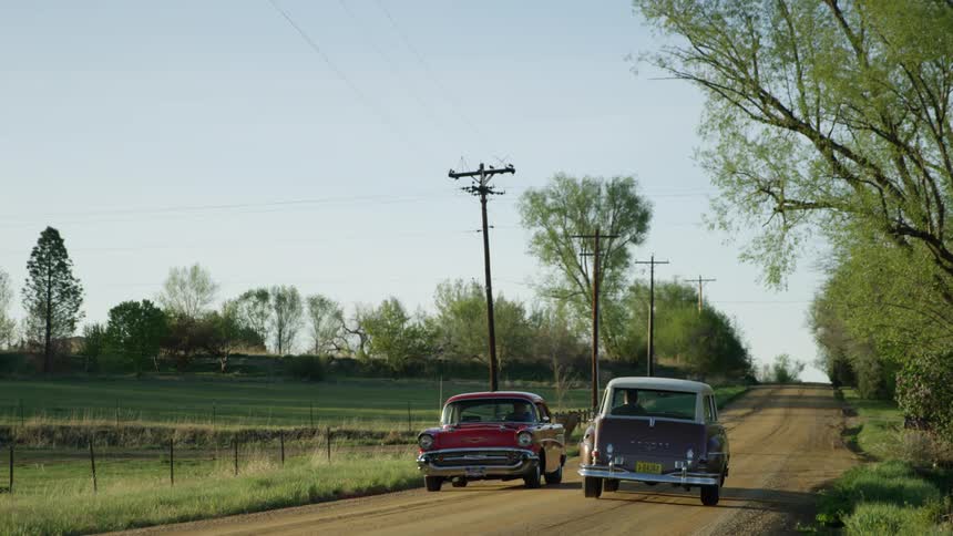 Classic cars driving along dirt country road in a rural area