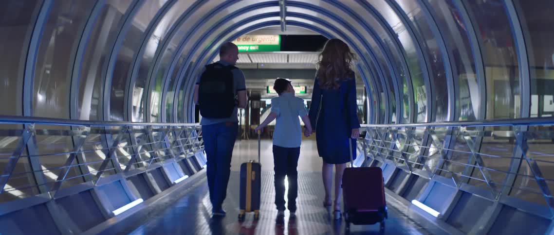 A family walks through a modern airport while pulling luggage behind them
