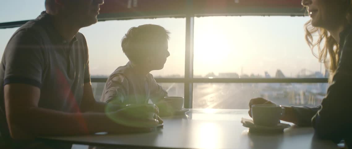 A family sits and has coffee while a young boy admires planes on the tarmac