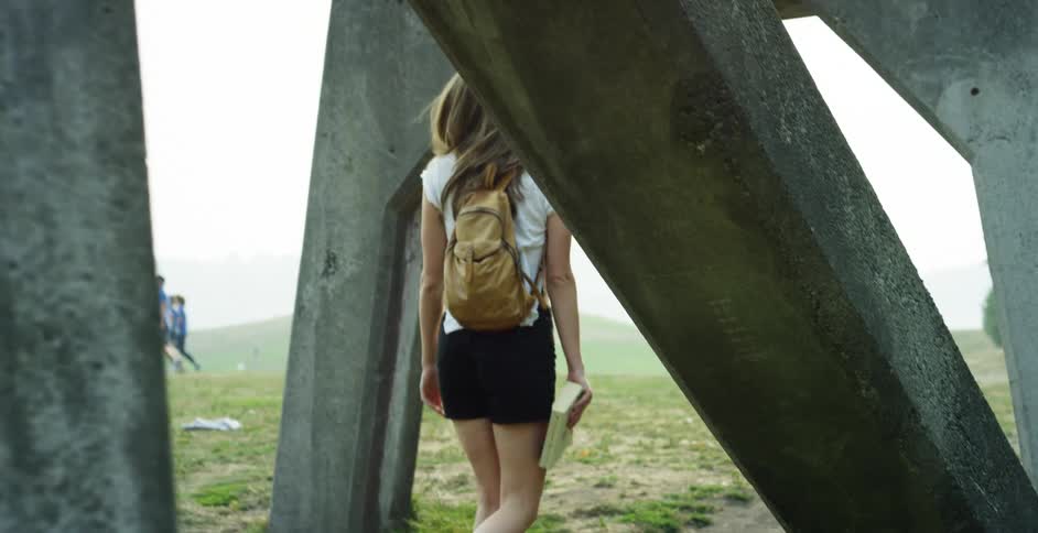 A female teenager walks along carrying a book and looks at a group of people walking past