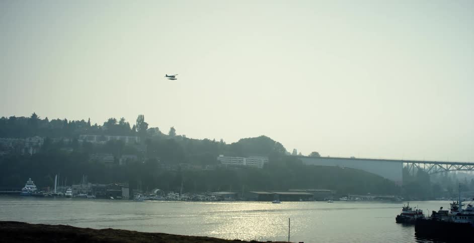 A sea plane flies over the harbor towards a bridge