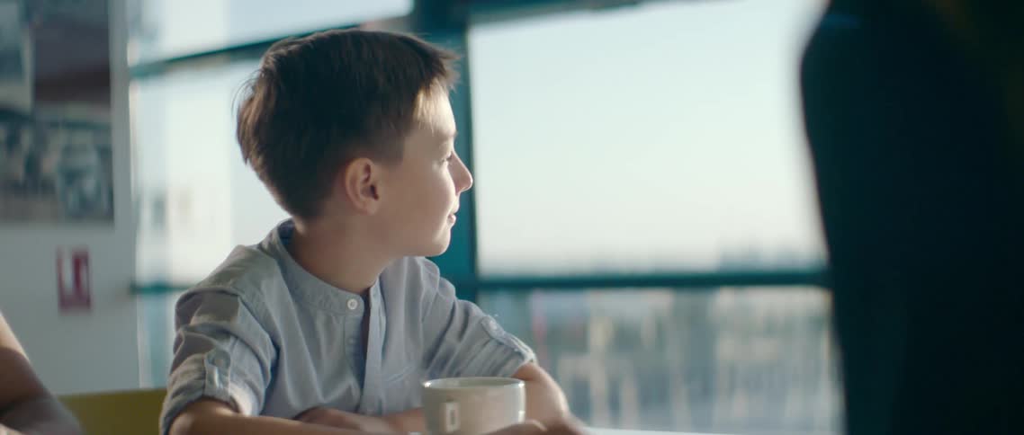 Kid sitting at the table looks out the windows and smiles slightly at the airport