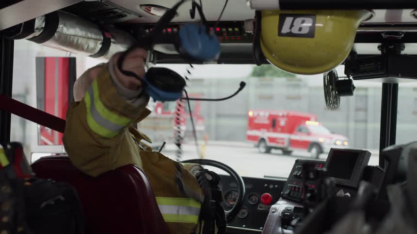 A firefighter sitting in the drivers seat of the fire engine takes his headset off as the ems unit approaches