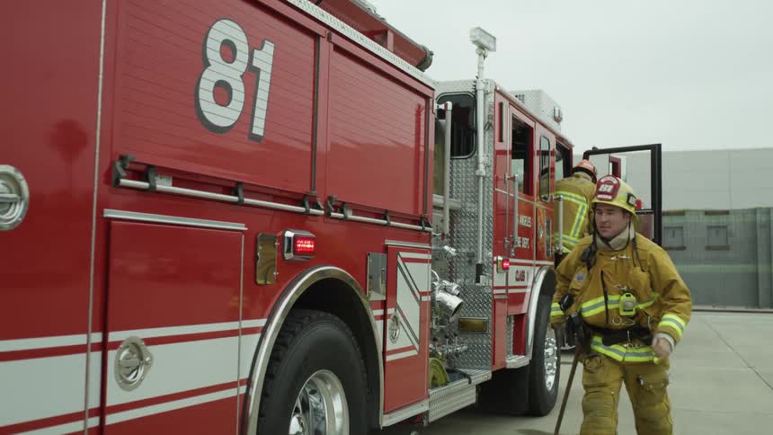 A firefighter gets out of a fire truck and opens a door at the back of the vehicle