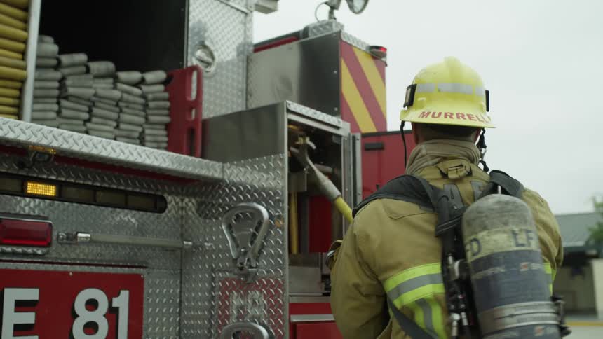 A firefighter removes a tool from the back of a fire engine and carries it around the vehicle