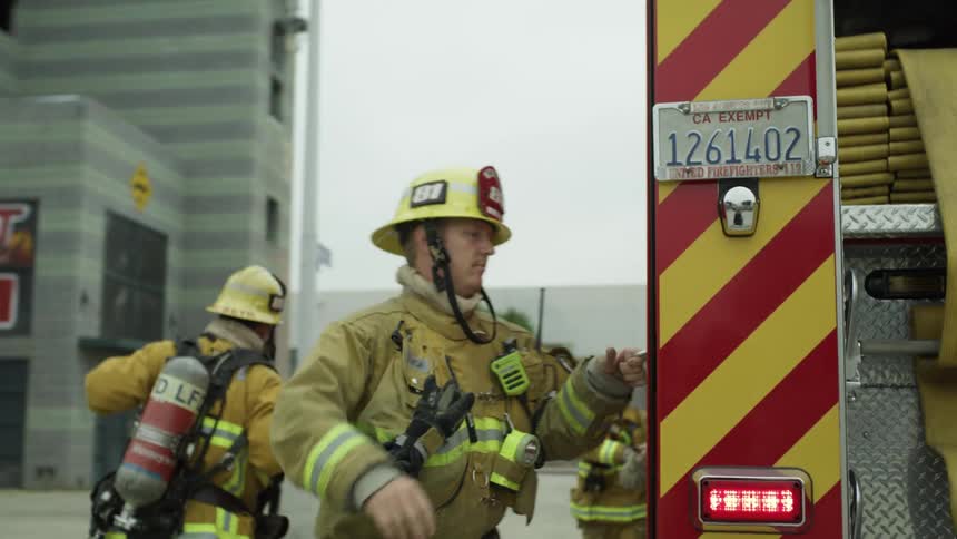 A group of fire fighters gearing up and gathering equipment outside of a building