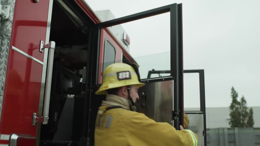 Firefighters step out of fire engine with blinking lights near buildings moving quickly