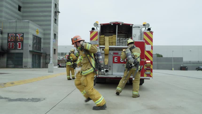 Firefighters suit up near their fire truck parked in front of a building