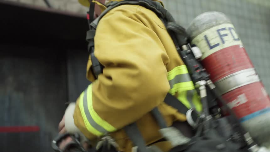 A firefighter with oxygen tank and helmet carrying a hose