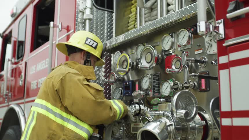 A firefighter hooks a hose up to a firetruck