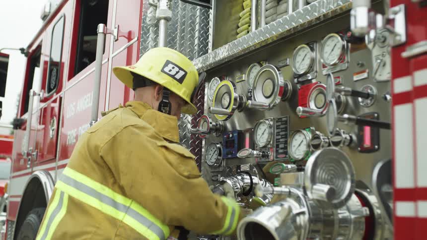 A fire fighter is using a hose from the fire truck