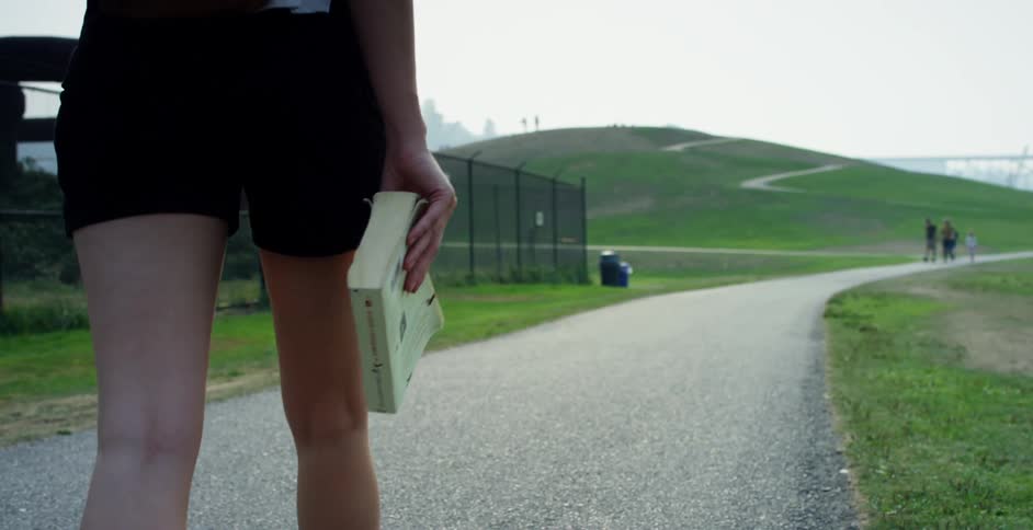 Woman with backpack holds a book and walks along a concrete road