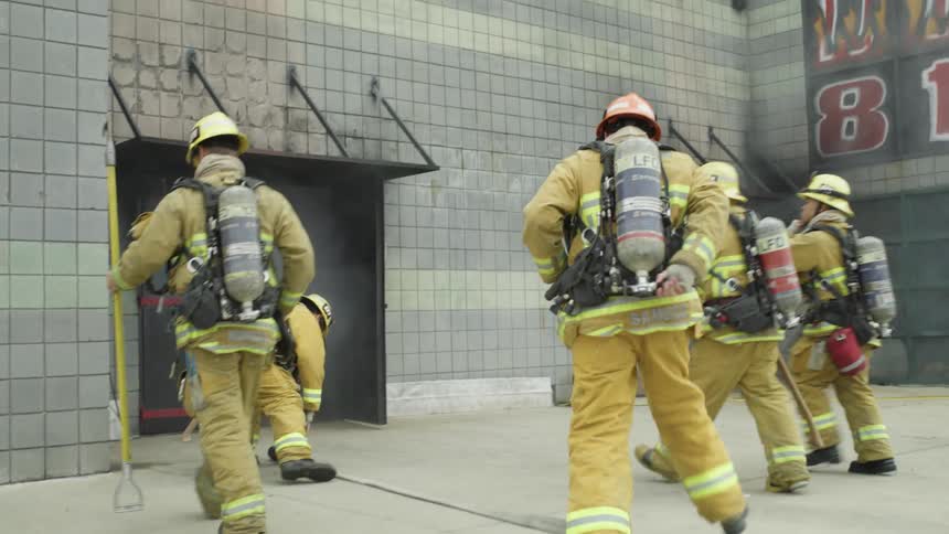 Firefighters run towards a building with smoke coming out the doors