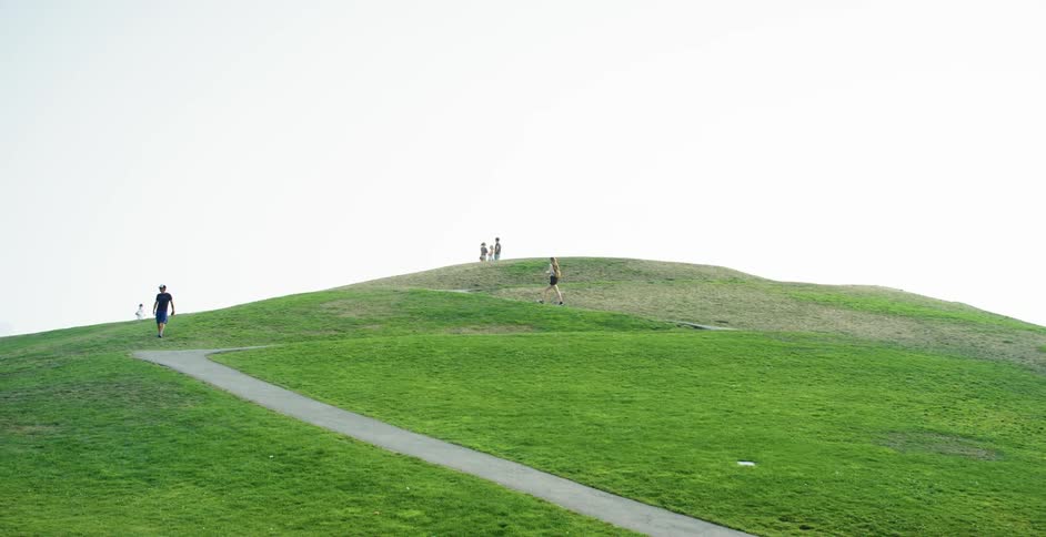 White people walk around a hill in a park