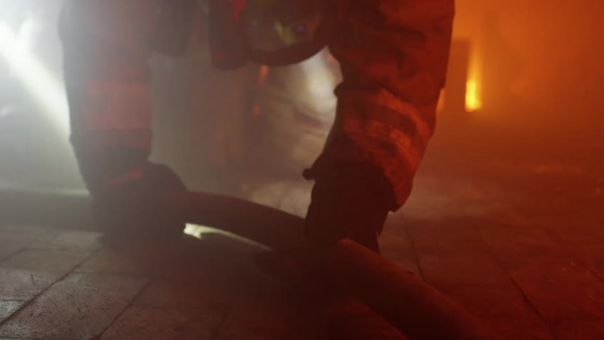 Firefighters crawl along the floor and grab onto a hose inside a building on fire