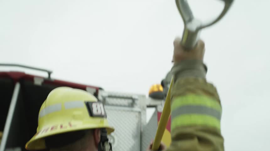 A firefighter in uniform takes a tool out of a fire truck