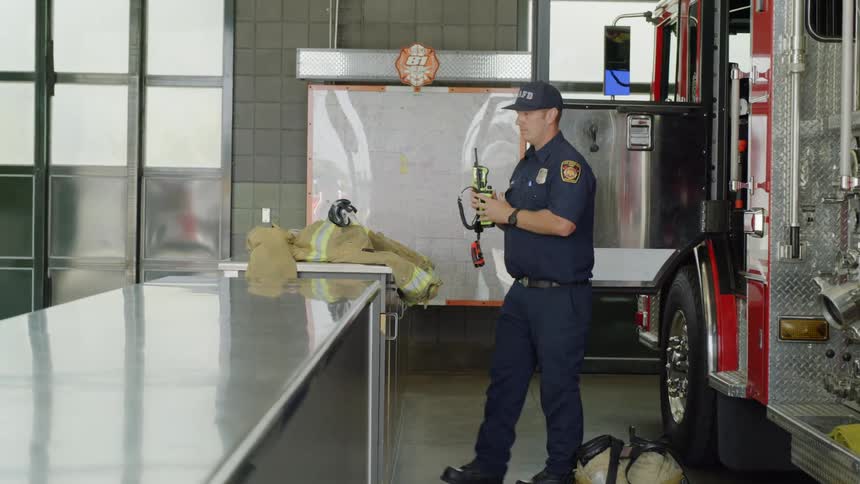 A firefighter in a station house takes gear out of a truck and places it on a counter