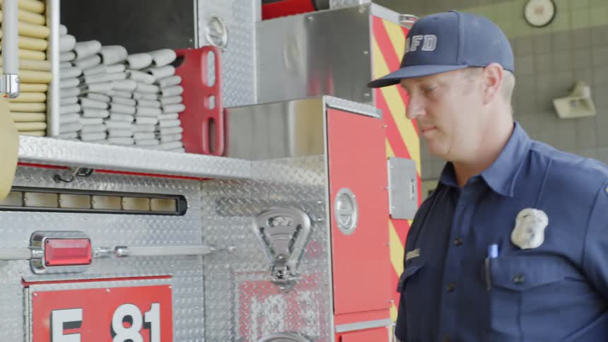 A firefighter carries his uniform past a fire truck