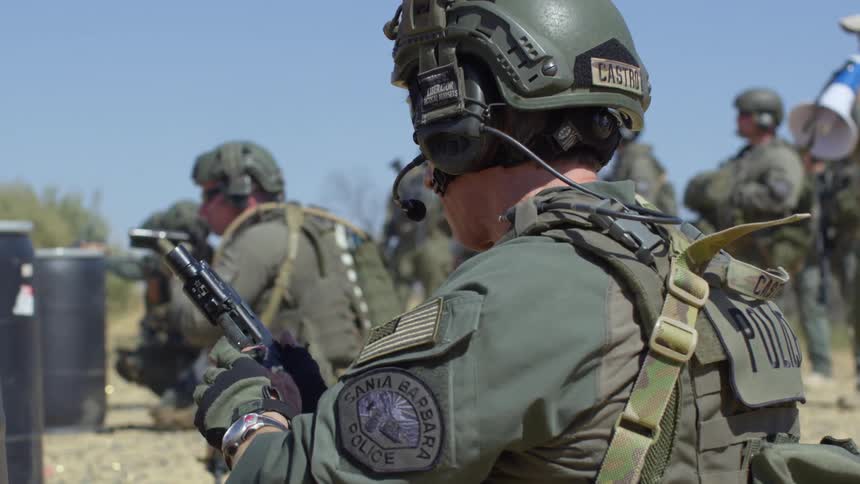 Police officer in armor loads clip into gun outside in field