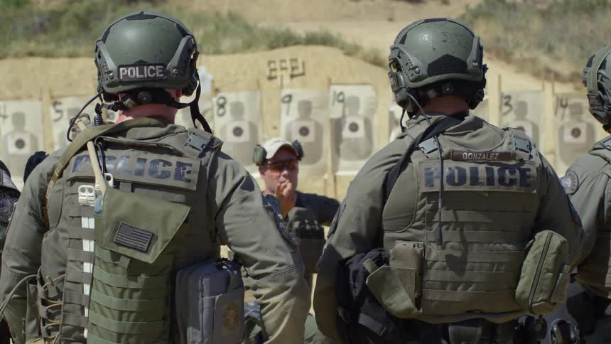 A group of military police at a shooting range listen to instructions from their superior