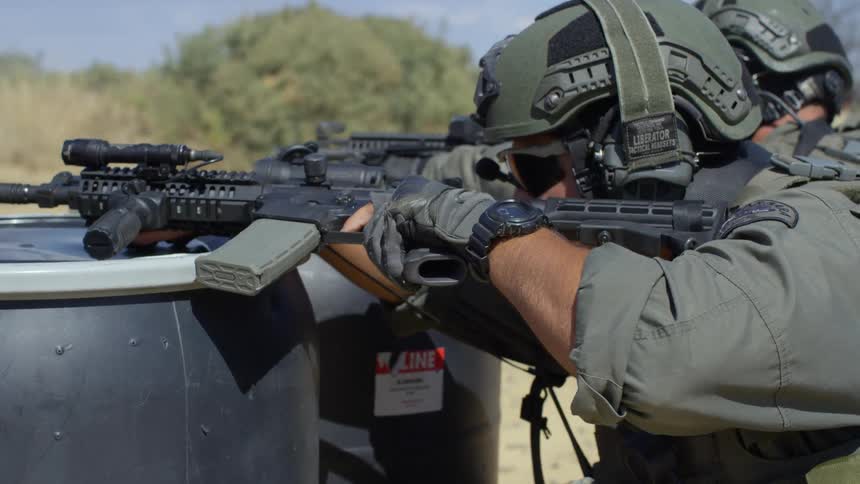 A pair of police officers kneeling behind black barrels while firing assault rifles