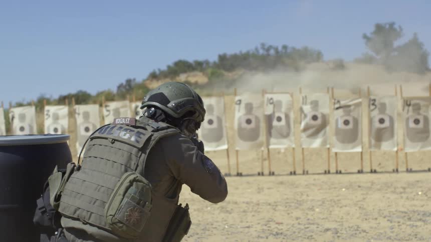 Police officers hide behind barrels as they shoot at paper targets during a swat training exercise