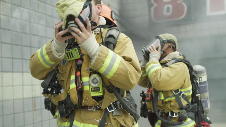 Firefighters with helmets and oxygen tanks putting on masks