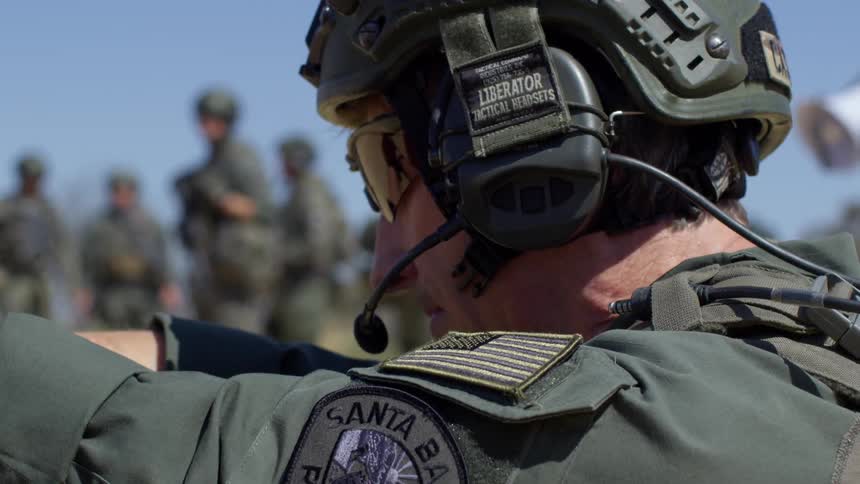 A police officer with a helmet sunglasses and a headset shooting a pistol