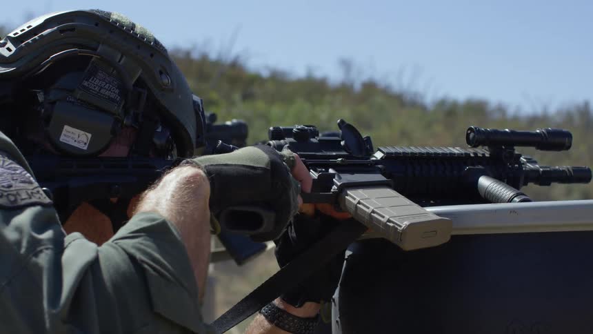 A police officer repeatedly fires a machine gun at a target