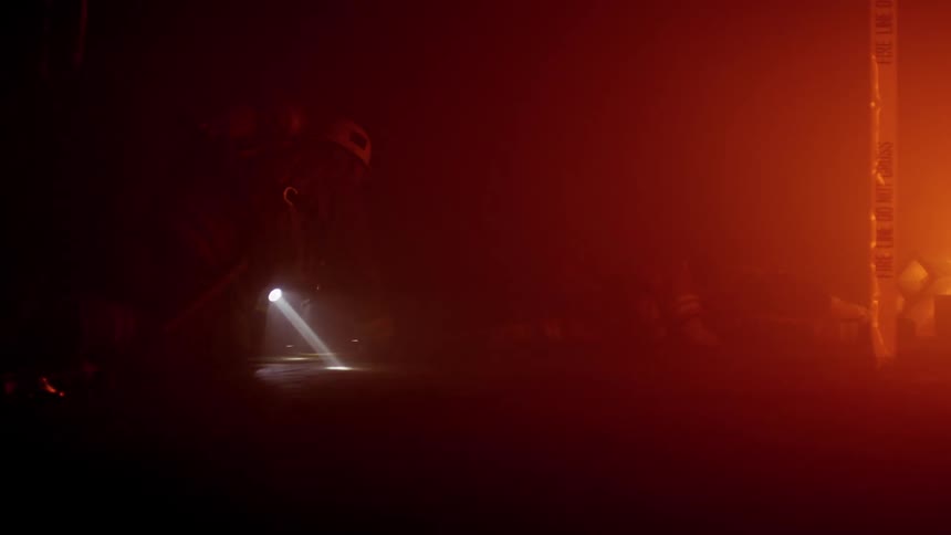 Three firefighters crawl to another lying on the floor of a burning building