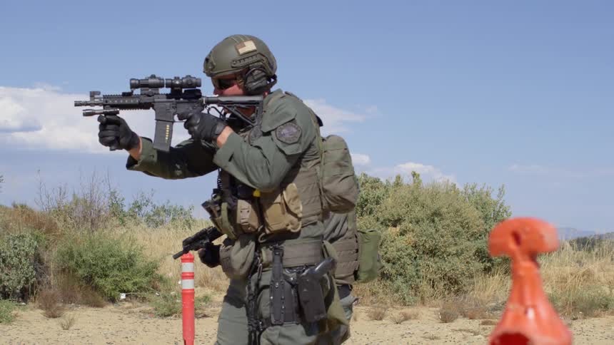 A pair of police officers brandishing and firing firearms while traversing a training course