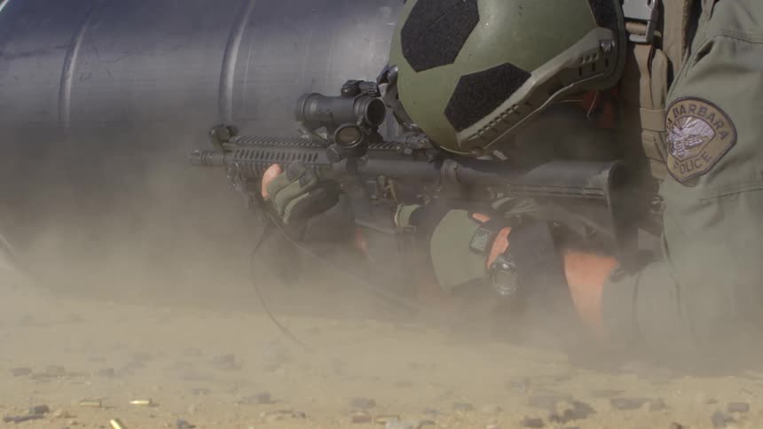 A policeman in combat gear lying prone while firing an assault rifle