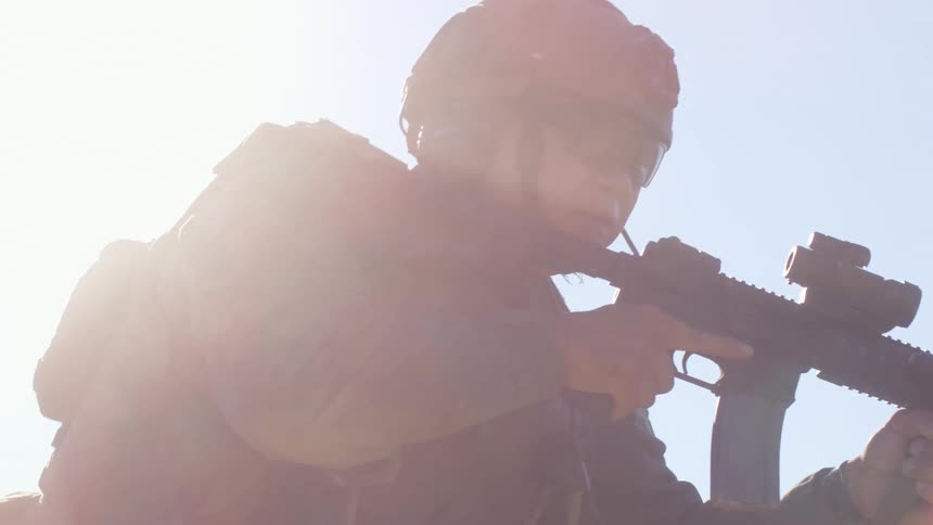 A police officer in tactical gear and carrying a rifle moves away from a barricade