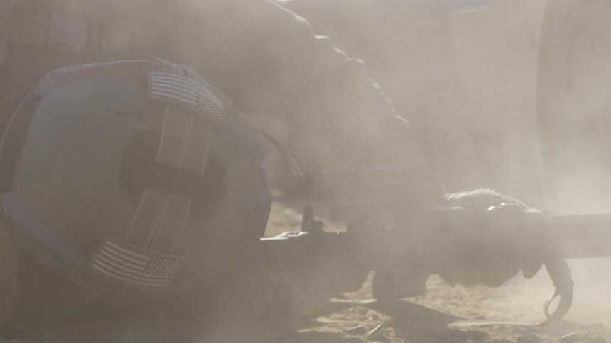 Soldier wearing helmet lies on side shooting rifle tossing dust into air