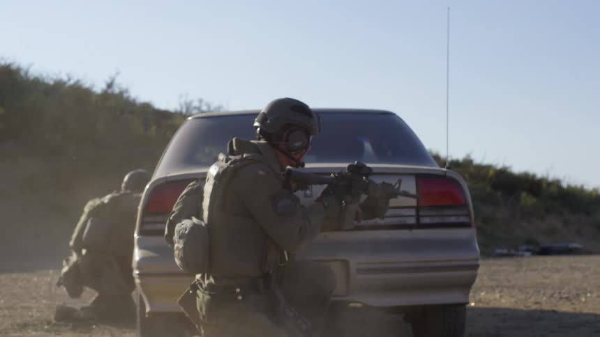 A armed soldier runs and hides behind a deserted vehicle