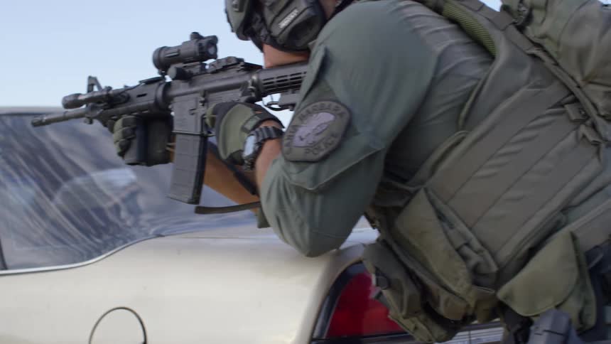 Police officer in a training exercise wearing combat gear and assault rifles take cover behind a car