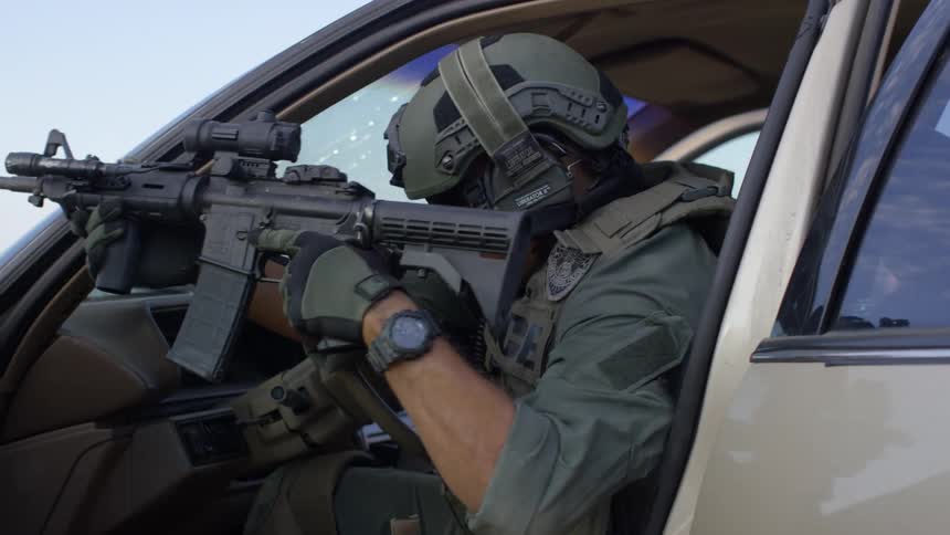A policeman opens his car door and shots a rifle