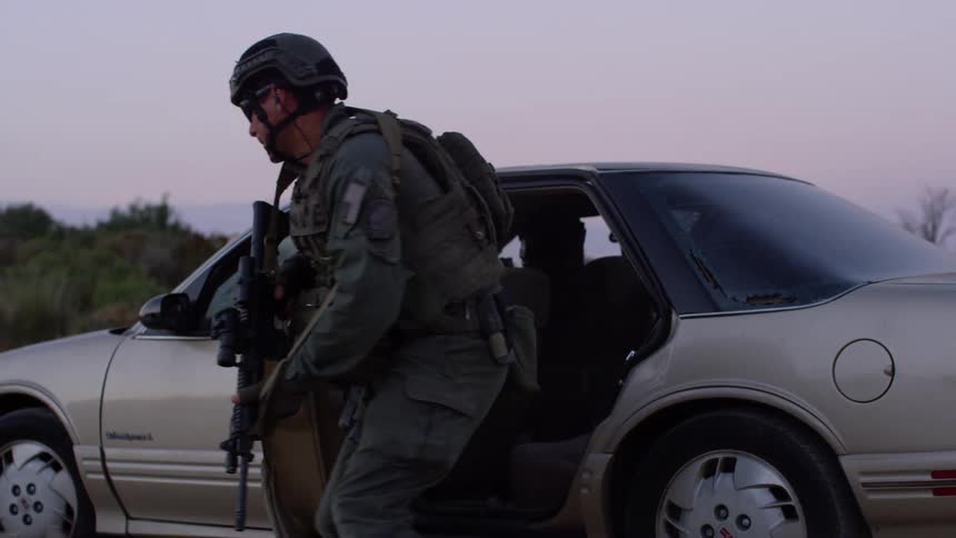 A police officer steps out of a vehicle with his gun drawn and shoots at a paper target in another vehicle during a drill