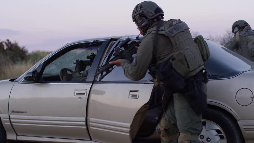 Police officers in military gear gets off a car and engages in a training exercise