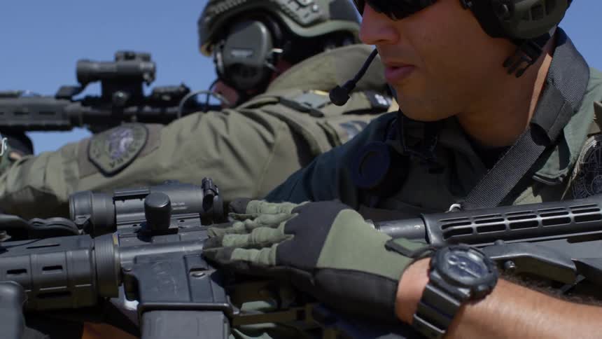 An officer with a helmet gloves and sunglasses loads a magazine into a rifle then shooting it