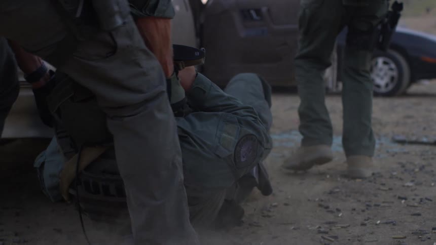 A soldier drags another soldier behind a car as another stands cover