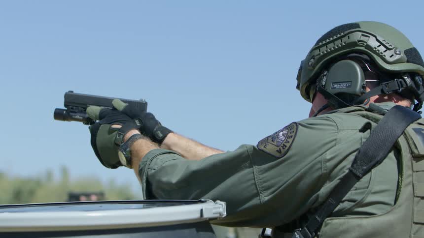 Man wearing body armor and helmet aims and shoots gun