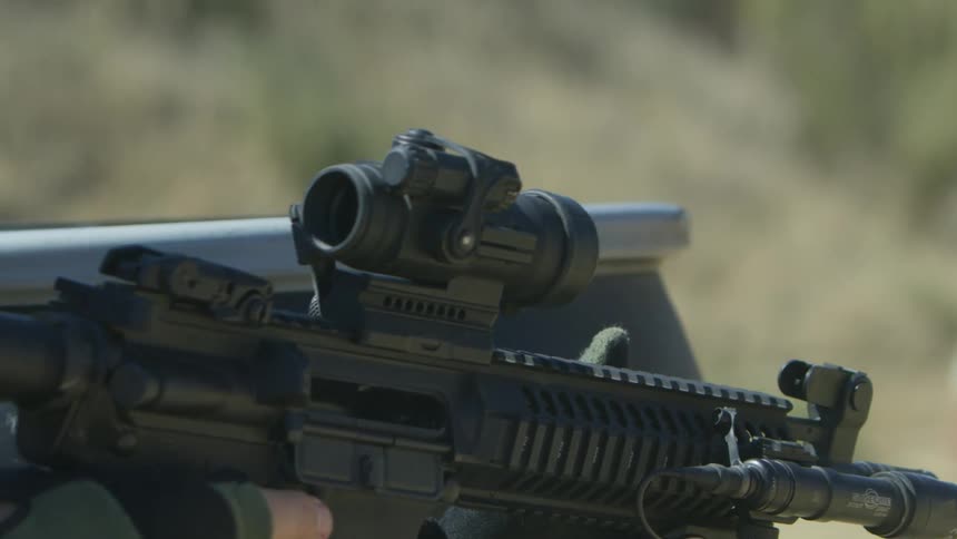 A person with gloves and a helmet shooting a rifle