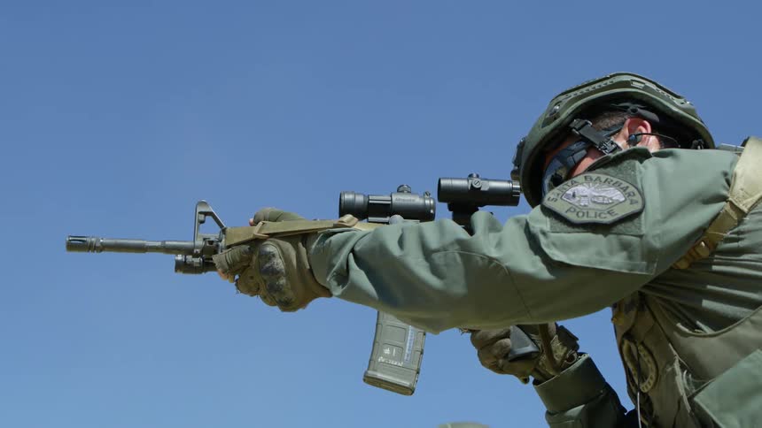 A police officer in green fatigues shoots at a target with a rifle