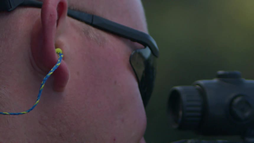 A soldier looks through a rifle scope and fires off a round